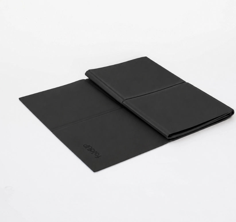 A black foldable yoga mat shown open and closed on a clean white background. The brand name 'foldup' is debossed on the lower left corner of the open section.