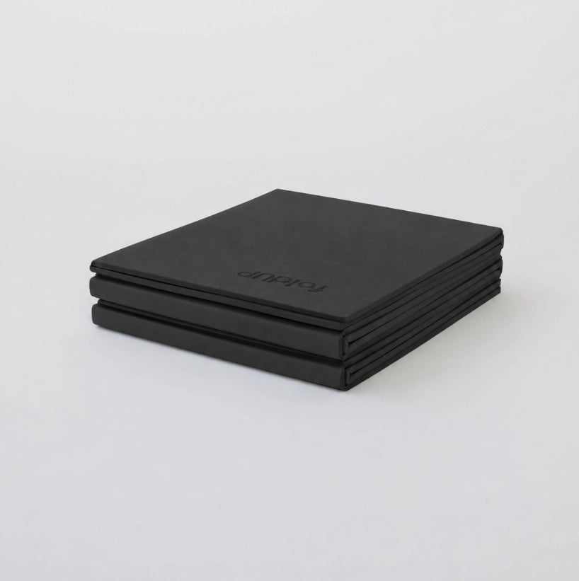 A folded yoga mat, featuring the debossed brand name 'foldUP' on the top piece, set against a clean white background.